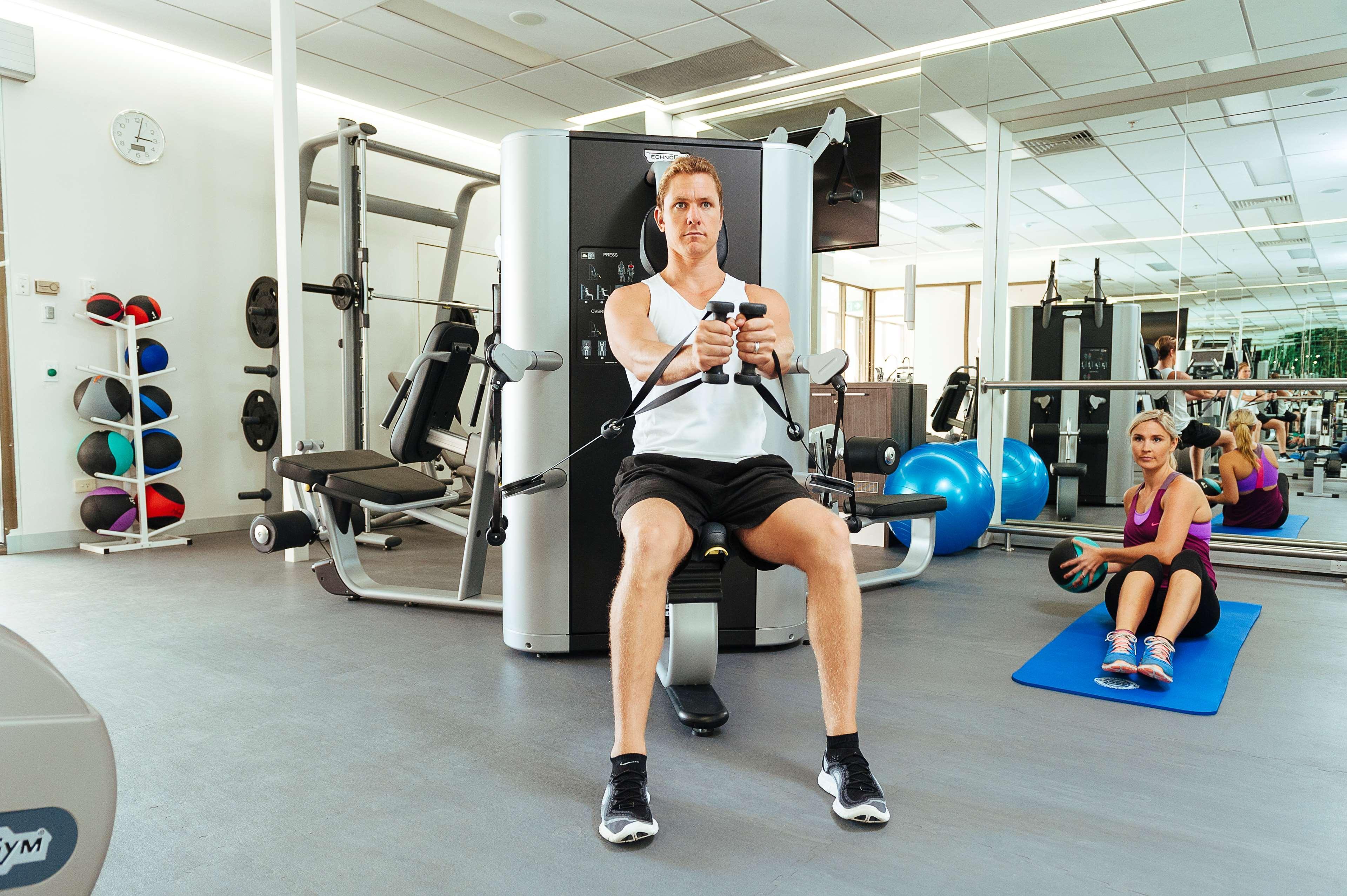 스탬퍼드 플라자 애들레이드 호텔 외부 사진 The photo shows a gym setting with two individuals engaged in workout activities. 

In the foreground, a man is seated on a machine, using the handles to perform a rowing exercise. He is wearing a sleeveless shirt and shorts, indicating an active wor