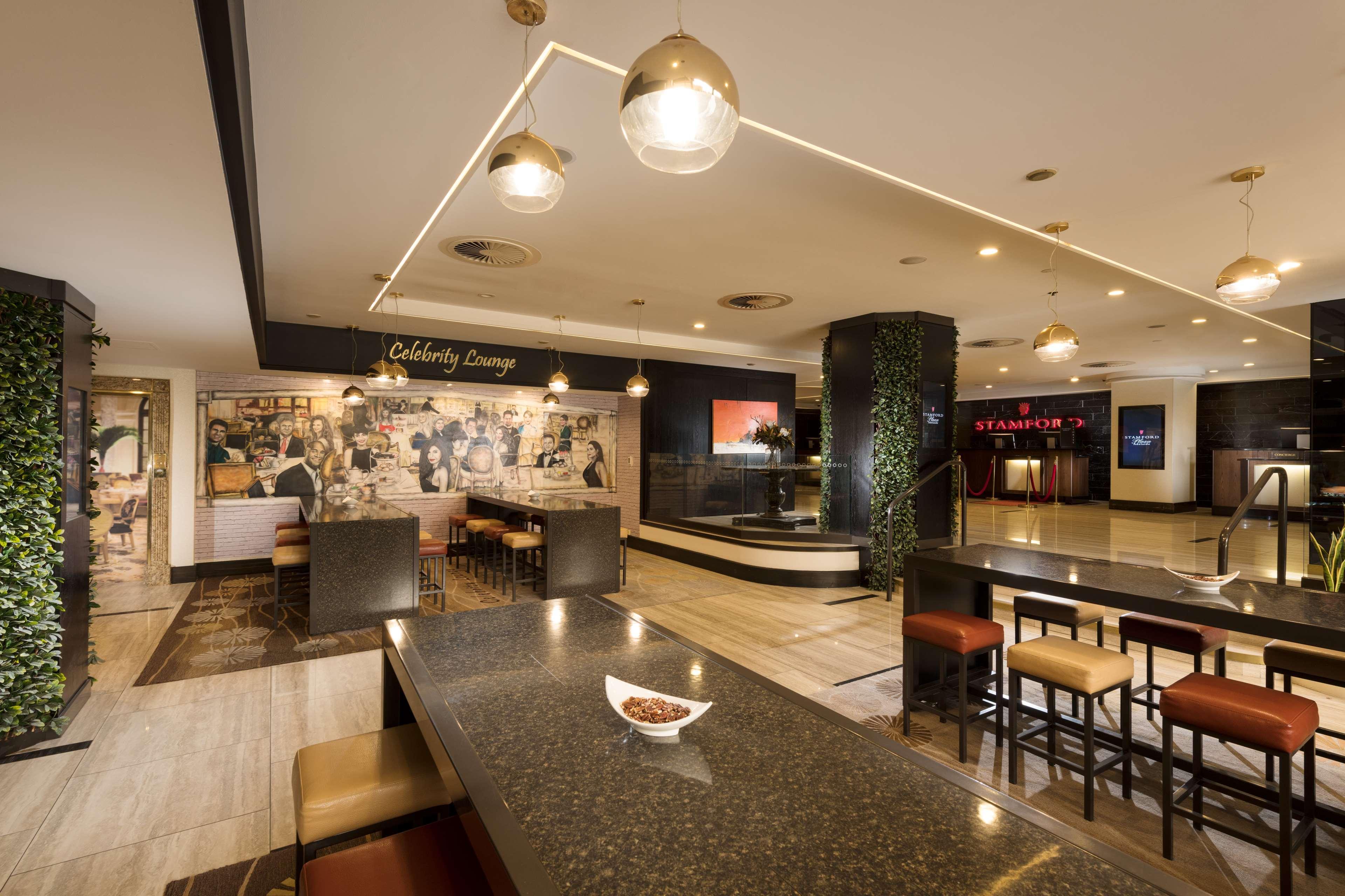 스탬퍼드 플라자 애들레이드 호텔 외부 사진 The photo shows a modern and stylish interior of a lounge or restaurant area. Prominent features include a long dark countertop with bar stools, and several pendant lights hanging from the ceiling. In the background, there is a mural or artwork that 