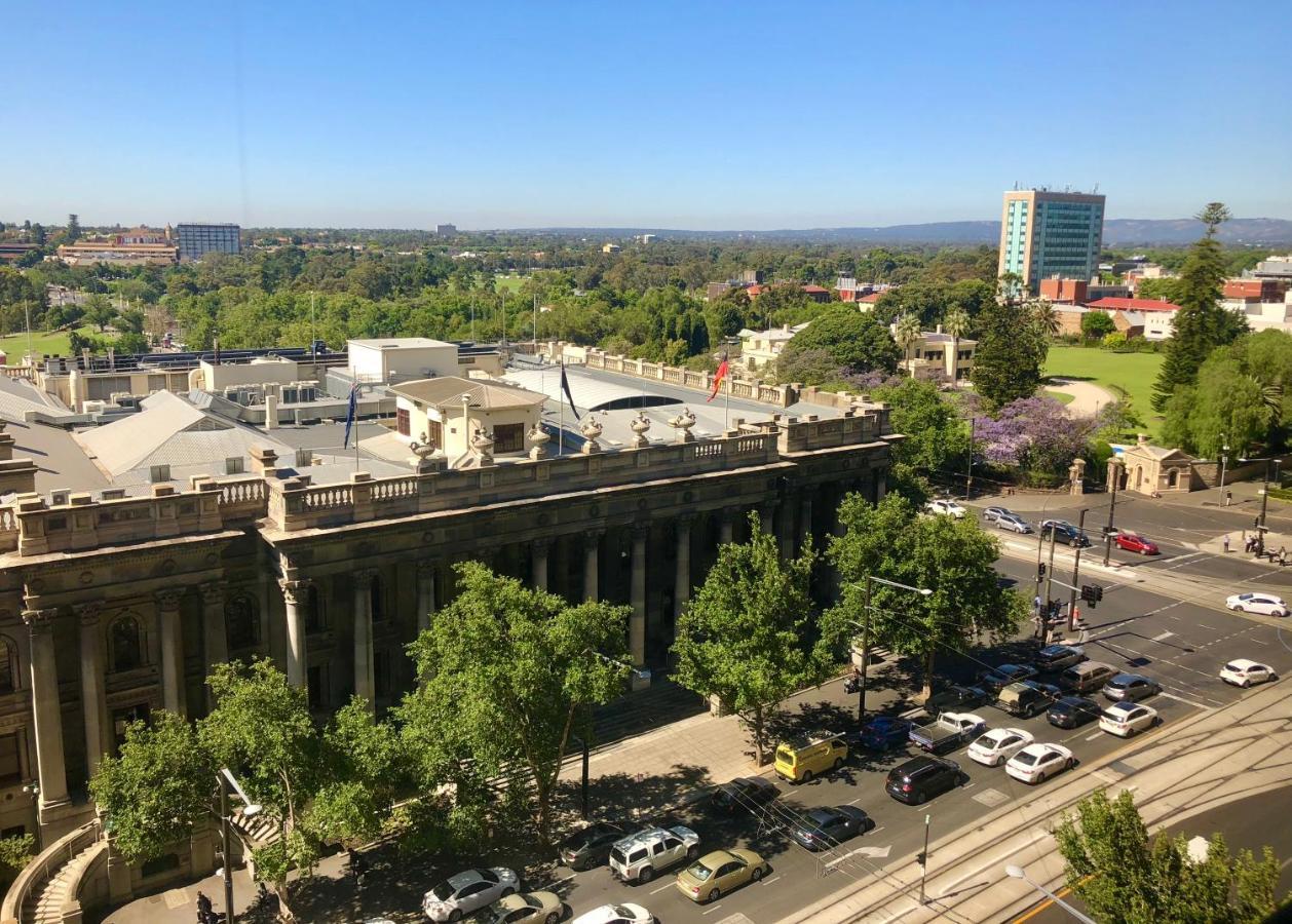 스탬퍼드 플라자 애들레이드 호텔 외부 사진 The photo depicts a cityscape view, showcasing a mix of architectural structures and greenery. In the foreground, there is a large, classical building with columns, suggesting it may be a historical or governmental structure. Surrounding the building